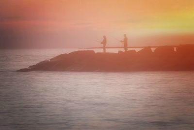 Silhouette people standing by sea against sky during sunset