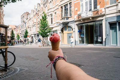 Cropped image of hand holding ice cream cone on cobbled street