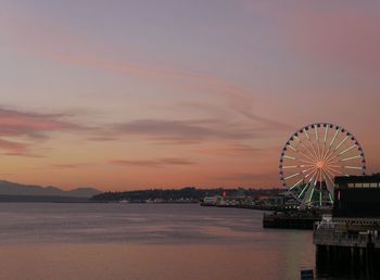 Ferris wheel by sea against sky at sunset