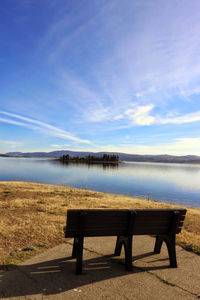 Bench by lake against blue sky