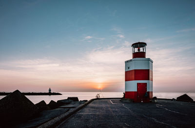 Lighthouse by sea against sky during sunset