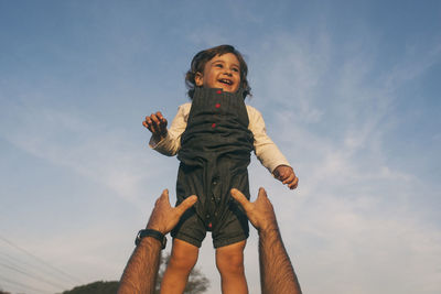 Cropped hands of father reaching daughter against sky