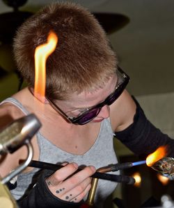 Young woman making glass with flaming torch in factory