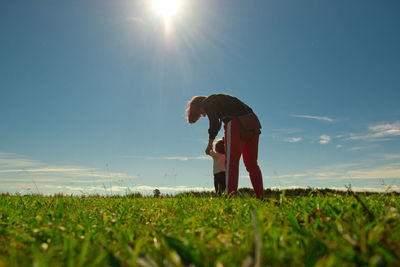 Low angle view of mother holding daughter walking on land against blue sky