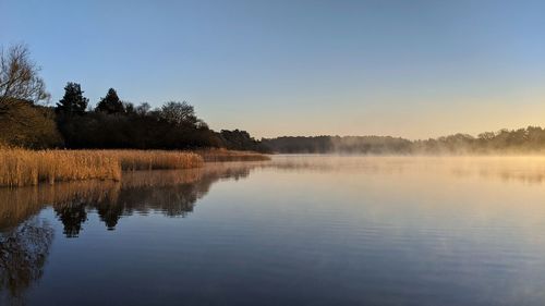 Scenic view of reflections of a foggy lake against clear sunrise sky