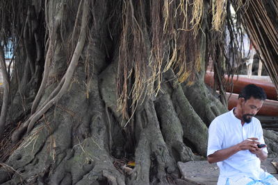 Man using mobile phone while sitting against trees