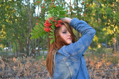 Portrait of young woman holding rowanberries while standing on field