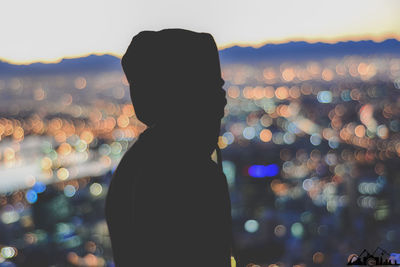 Rear view of silhouette man standing against illuminated sky at dusk