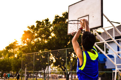 Man reaching basketball hoop against sky