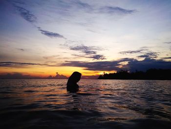 Silhouette person swimming in sea against sky during sunset