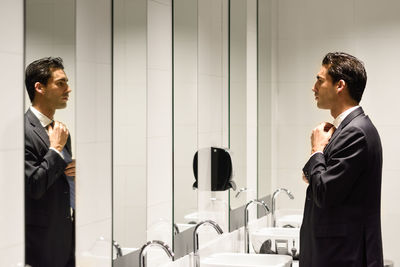 Side view of businessman adjusting tie in restroom