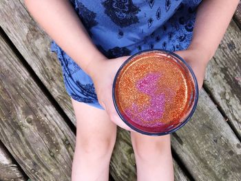 Midsection of woman holding glitter while sitting on wood