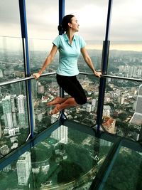 Woman balancing on railing over glass floor at menara kuala lumpur tower