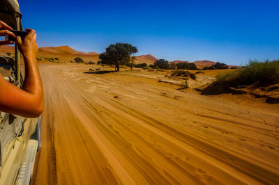 Cropped image of hand photographing while traveling in vehicle at desert