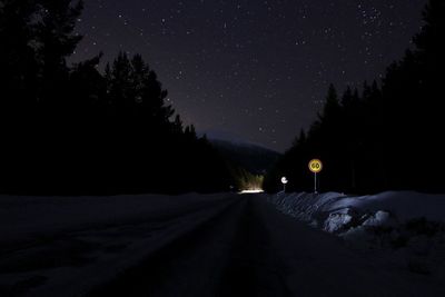 Road amidst trees against sky at night during winter