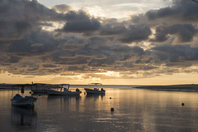 Sailboats moored on sea against sky during sunset