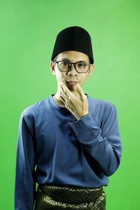 Portrait of young man standing against green background
