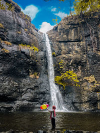 Woman holding balloons while standing against waterfall