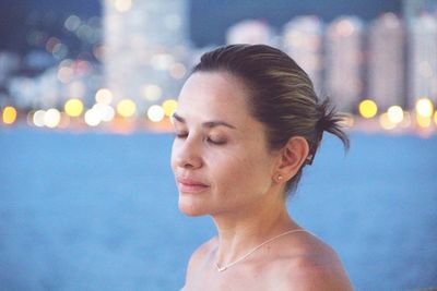 Close-up of shirtless woman with eyes closed standing against sea