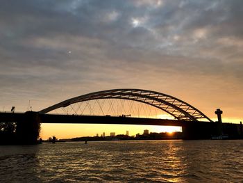 Silhouette bridge over river against sky during sunset