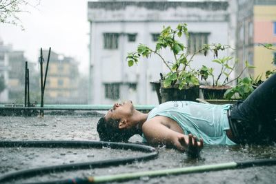 Young man lying on street in city during rainy season