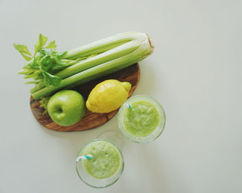 Directly above shot of drink and vegetables with fruits against white background