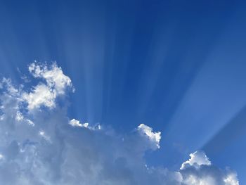 Low angle view of sunlight streaming through clouds