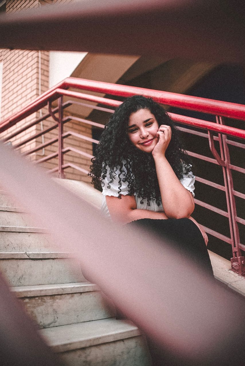 PORTRAIT OF YOUNG WOMAN SITTING ON STAIRCASE