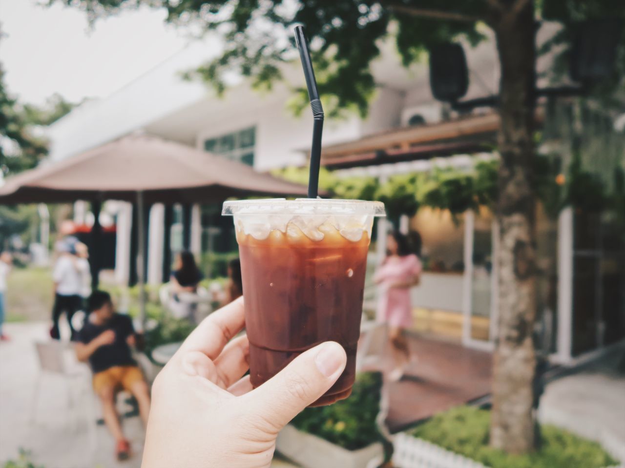 human hand, holding, food and drink, hand, refreshment, focus on foreground, drink, one person, real people, drinking glass, lifestyles, household equipment, glass, human body part, architecture, drinking straw, freshness, straw, close-up, unrecognizable person, finger, outdoors, cocktail