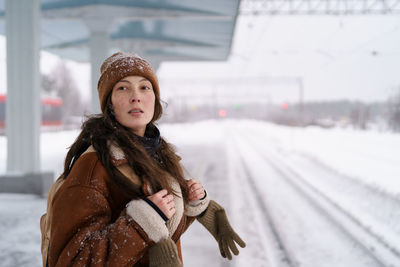 Thoughtful woman with backpack standing on snow-covered platform and looking at arriving train