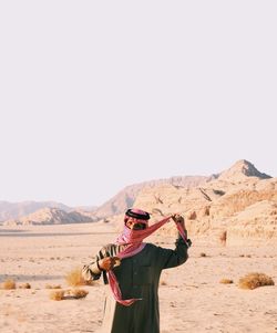 Rear view of young woman standing on desert against clear sky