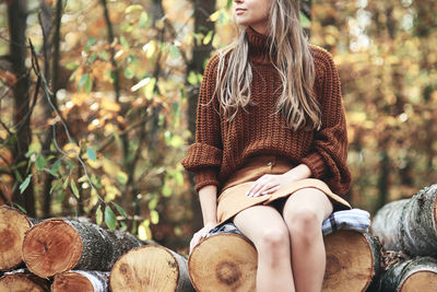 Midsection of woman sitting on log in forest