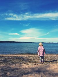 Rear view of woman standing on beach against sky