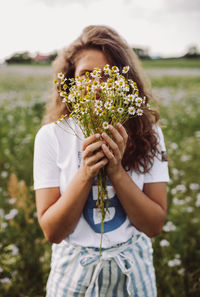 Midsection of woman holding flowering plant on field