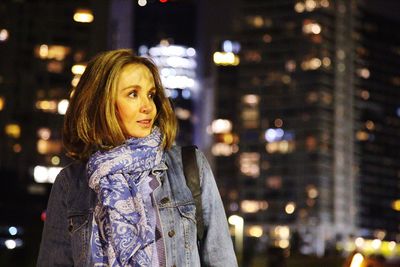 Woman standing against illuminated city at night