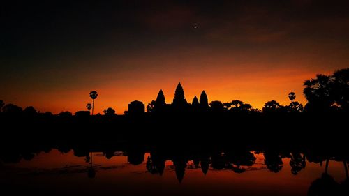 Silhouette temple by lake against sky during sunset