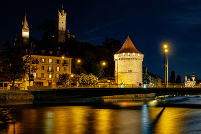 Illuminated bridge over river against buildings in city at night