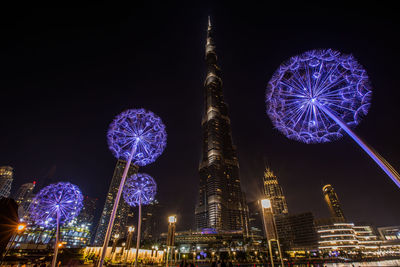 Low angle view of illuminated ferris wheel against buildings at night