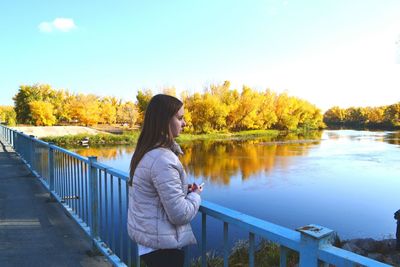 Side view of thoughtful woman standing on footbridge over lake