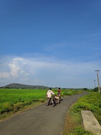 Rear view of people riding motorcycle on road against sky