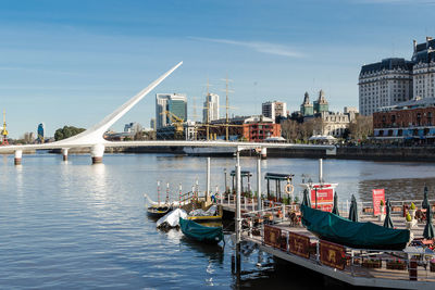 Sailboats moored on river by buildings against sky in city