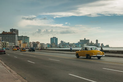 Cars on city street by buildings against sky