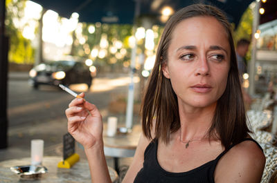 Portrait of young woman holding cigarette at restaurant table