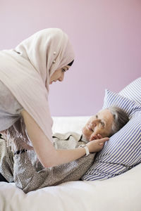 Young female home caregiver assisting senior woman in bed