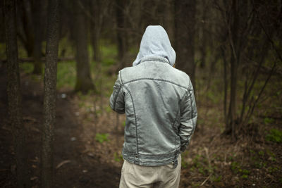 The guy in the hood is taken off the back. a man in jeans stands in the woods. 