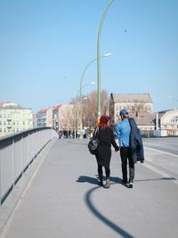 Full length rear view of couple walking on bridge against sky