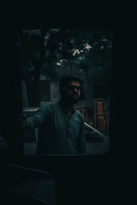 Young man looking through window at night