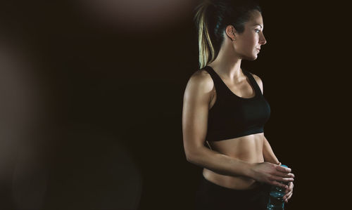 Athlete woman holding water bottle against black background