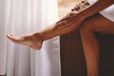 Low section of woman applying moisturizer on leg