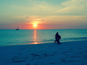 Silhouette boys playing at beach against sky during sunset